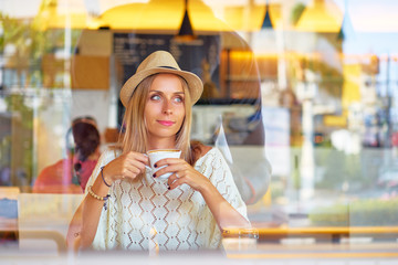 Drinking tea. Pretty young woman in hat holding cup of beverage while sitting at cafe.