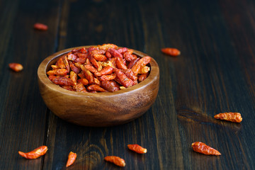Dried bird's eye chili peppers in a wooden bowl. Dark wooden table, high resolution