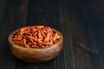 Dried bird's eye chili peppers in a wooden bowl. Dark wooden table, high resolution, negative space