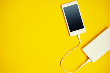 Smartphone charging with power bank on yellow background.