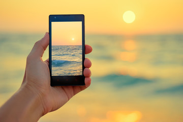 Cell technology and vacation. Close up of male hand holding smartphone, taking picture of sea sunset.