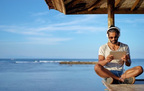 Relaxed and cheerful. Work and vacation. Outdoor portrait of happy young african man using tablet computer on deck near the sea.