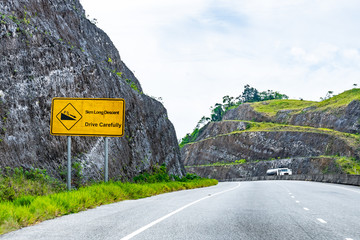 Yellow Caution 5km Long Descent downhill 8% decline street traffic arrow symbol sign on dual carriageway highway through scenic mountain countryside where cars drive on left hand side of the road.