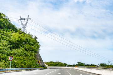 80 km/h speed limit and Falling Mountain Rocks/Rock Slide street traffic sign with HDVC lines overhead on dual carriageway highway through scenic countryside where cars drive on left hand side of road