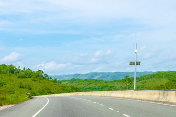 Fototapeta na wymiar Energy efficient solar powered security system street camera on dual carriageway highway through mountain landscape. Vehicles drive on left hand side of this two lane asphalt road in St Ann, Jamaica.