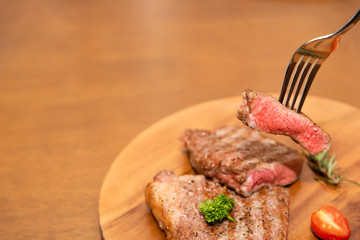 Cooked beef steak with rosemary, parsley and cherry tomato on fork, Wood background, Copy space on the left