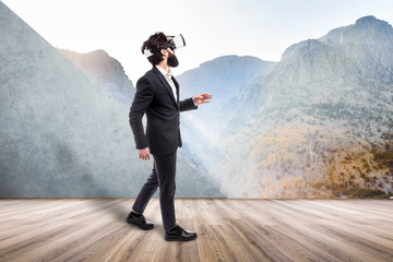 bearded man in VR glasses goes from an empty room into a non-existent virtual mountain landscape, concept of new technologies and virtual reality