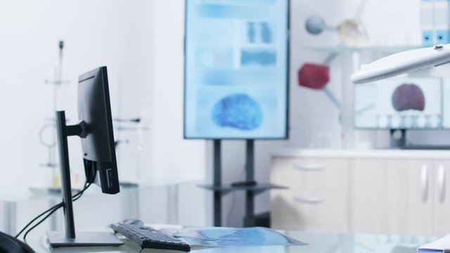 Desk in front of modern laboratory. Monitors in the background are displaying 3D brain and DNA scans