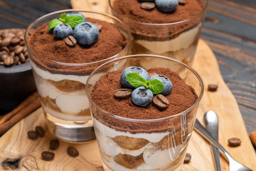 Classic tiramisu dessert in a glass with blueberries on wooden background