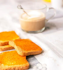group of biscuits with jam spread with a cup of cappuccino on a table with the decorated tablecloth