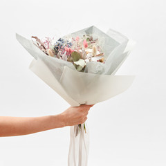Greeting bouquet from flowers in a hand on a light backhround.