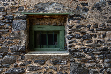 Old green window with bars in stone wall