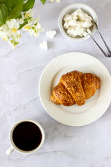 A croissant and coffee on a marble background. The flowers. Breakfast.
