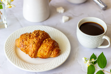 A croissant and coffee on a marble background. The flowers. Breakfast.