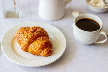 A croissant and coffee on a marble background. The flowers. Breakfast.