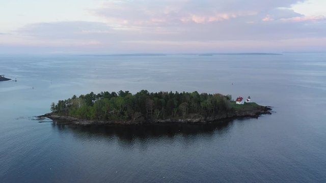 Slide past Curtis Island Lighthouse with pink sunset clouds in the background AERIAL