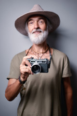 Traveler and photographer. Studio portrait of handsome senior man with gray beard and hat holding photocamera.