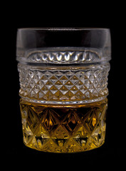 Illuminated crystal glass filled with golden whiskey on a black background.