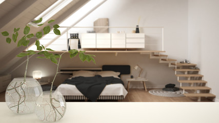 White table top or shelf with glass vase with hydroponic plant, ornament, root of plant in water, branch in vase, house plant, modern blurred bedroom in the background, interior design