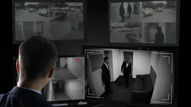 Male security operator watching surveillance cameras, illegal business deal