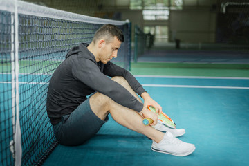 male tennis player sitting on the court. athlete holding a racket. sportsman has adjusted, lost and holds his head.