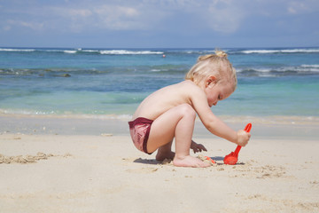 Little toddler girl playing with sand at the beach 