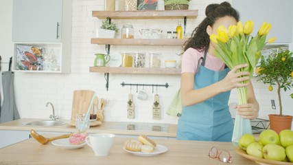 Young woman is putting flowers in a vase on the dining table
