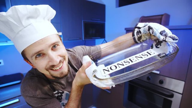 Cook baking nonsense in glass baking dish 4K. Wide view close-up on person face and dish in focus, smiling into the camera with kitchen in the background out of focus.