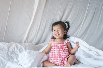 Closeup a little girl is sitting laughing on the bed in bedroom background