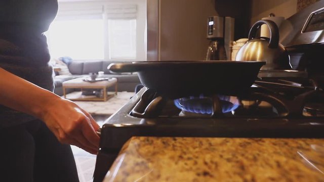 Slow motion close-up shot of a lady turning on the stove under a cast iron skillet pan in a kitchen