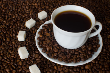 close-up of white Cup and saucer with black hot strong coffee Americano on a dark background of coffee beans with five pieces of white sugar refined. Flatlay