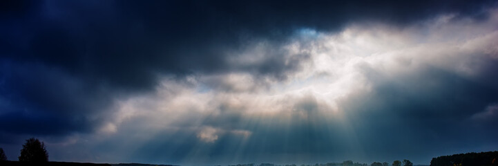 dark rainy sky and bright sun rays against the background of clouds.