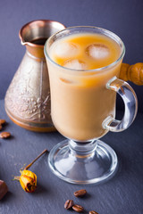 Copper coffee pot (Cezve) and coffee beans. Coffee with milk on dark background. Latte and black chocolate on slate board. Milk drink in glass beaker and dried rose