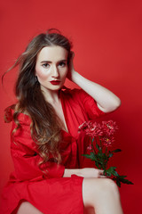 Romantic woman with long blonde hair and flowers in her hands in a red dress, smooth clean skin