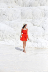 Woman in a red dress stands on white travertines. Girl in the sun near the white wall. Pamukkale