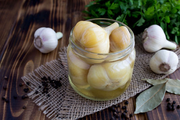 Pickled garlic in the glass jar on the rustic wooden background.Homemade fermented product.