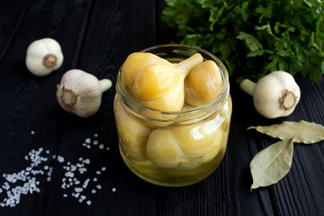 Pickled garlic in the glass jar on the black wooden background.Homemade fermented product.