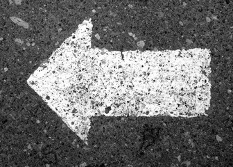 Left pointing arrow on asphalt in black and white.