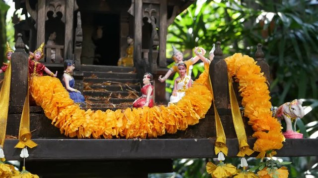 Wooden miniature guardian spirit house. Small buddhist temple shrine, colorful flower garlands. San phra phum erected to bring fortune. Traditional respect animistic rituals, pray ceremonies.