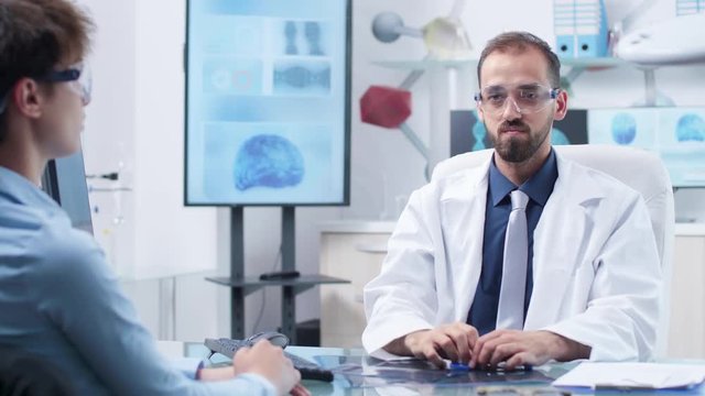 Doctor with AR glasses showing something to a patient. In the background - modern and high end research facility with screens running brain simulations