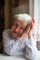 An old russian grandmother is sitting at a table in her house.