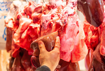 Fresh liver of lamb, sheep, pork, beef hanged on hooks. Butcher's hand show the product. Uncooked offal  for background, closeup.