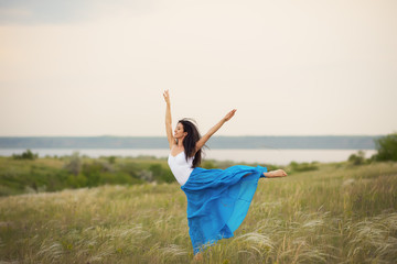 Classical dancer woman. Charming ballerina with windy hair in blue chiffon skirt dancing by the sea background. Sun shines on her. Horizontal.