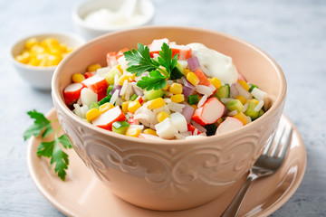 Salad with crab sticks, sweet corn, cucumbers, boiled eggs, onion and rice in bowl on concrete background. Russian cuisine. Selective focus.