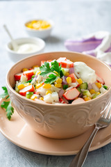 Salad with crab sticks, sweet corn, cucumbers, boiled eggs, onion and rice in bowl on concrete background. Russian cuisine. Selective focus.