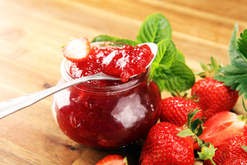 strawberry jam with fresh strawberries and mint. marmalade on spoon and jar on brown wood