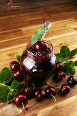 Rustic jar with cherry jam and fresh cherries, homemade preserves on wood