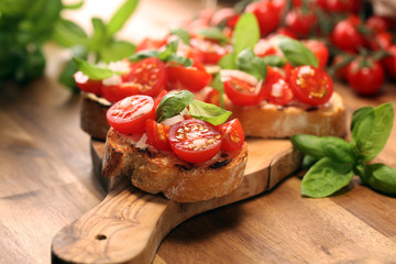 Traditional italian antipasto bruschetta appetizer with cherry tomatoes, cream cheese, basil leaves and balsamic vinegar on cutting board. Antipasti