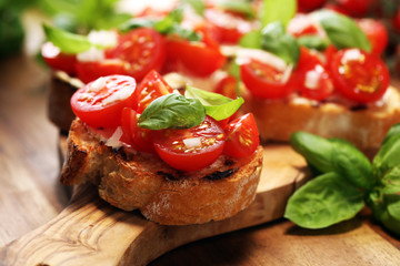 Traditional italian antipasto bruschetta appetizer with cherry tomatoes, cream cheese, basil leaves and balsamic vinegar on cutting board. Antipasti