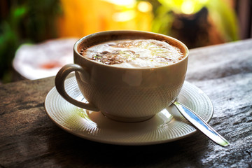 a cup of hot coffee in warm sunlight ambient on brown wooden table.